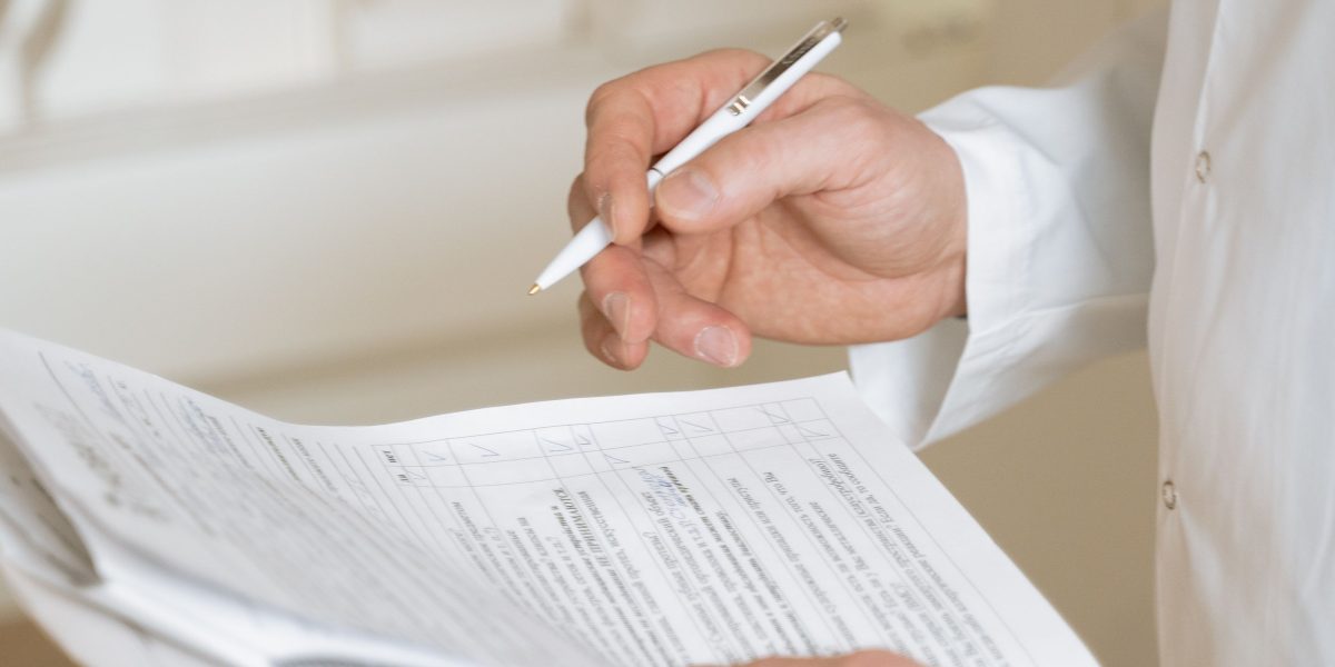 A professional carefully reviewing a document, possibly a checklist or report, related to compliance.