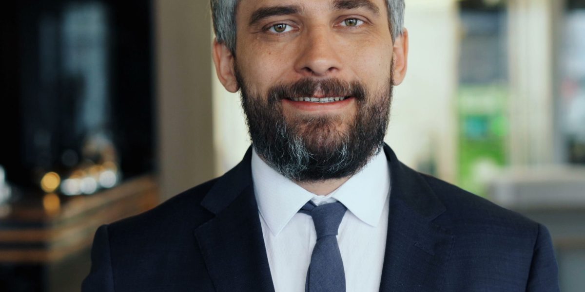 A confident hotel manager smiling in a modern hotel lobby, reflecting the efficiency and positive guest experience enabled by technology.