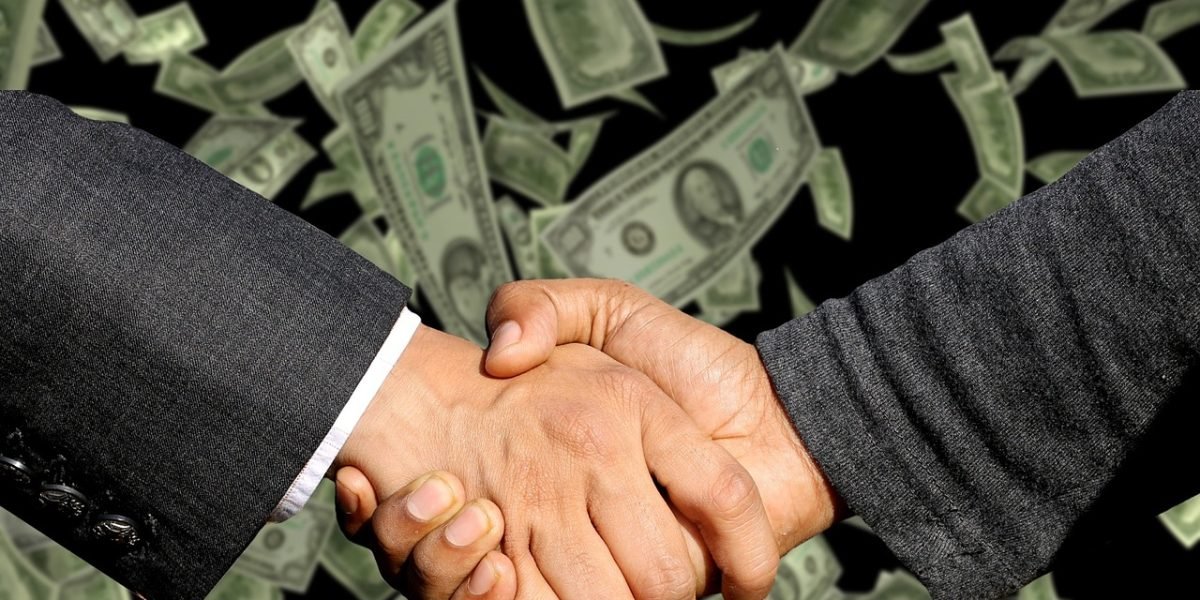 Business professionals in a meeting, shaking hands after negotiating a deal, reflecting investment implications.